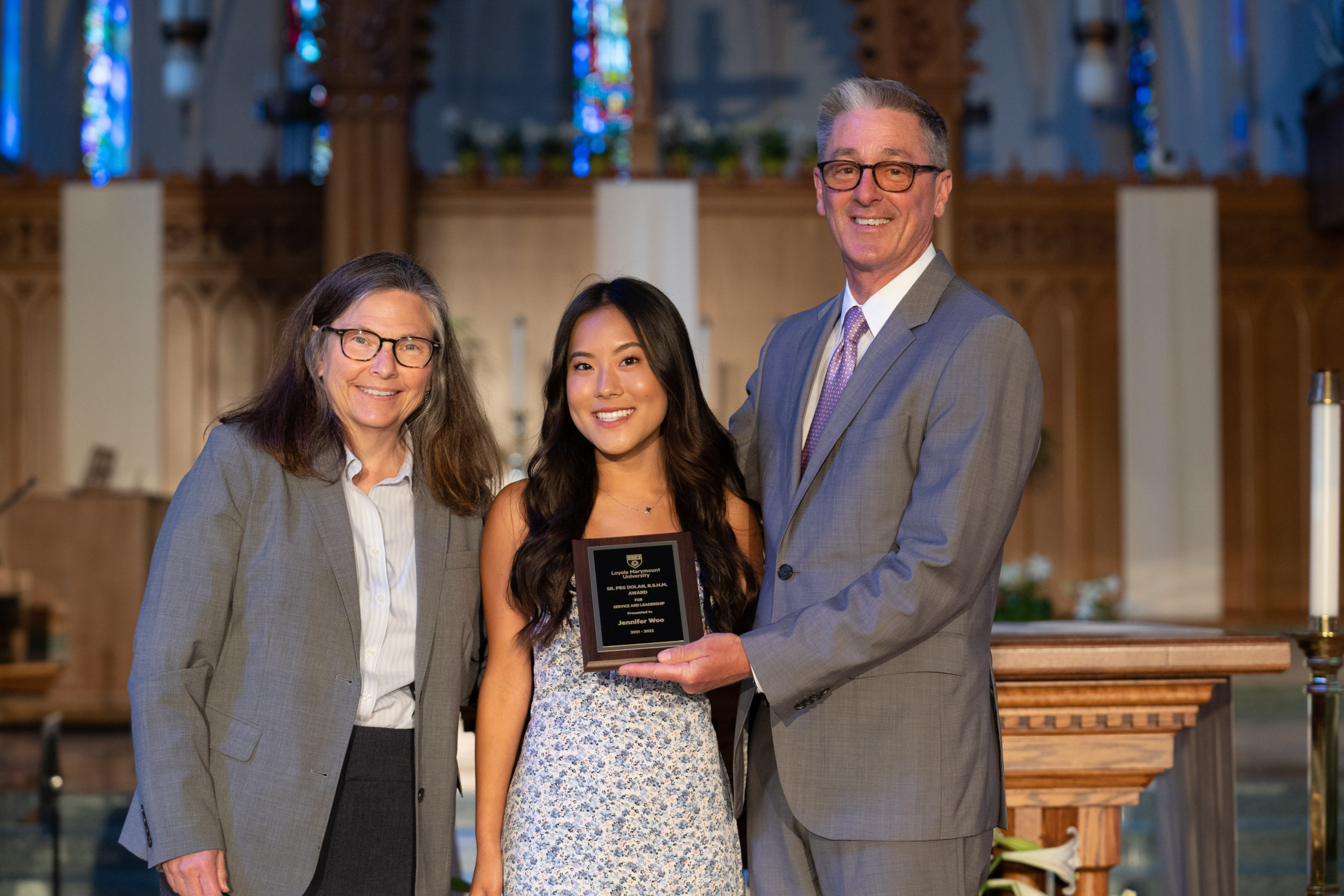 A student stands with two staff members from LMU inside the chapel to receive a Student Service and Leadership Award.